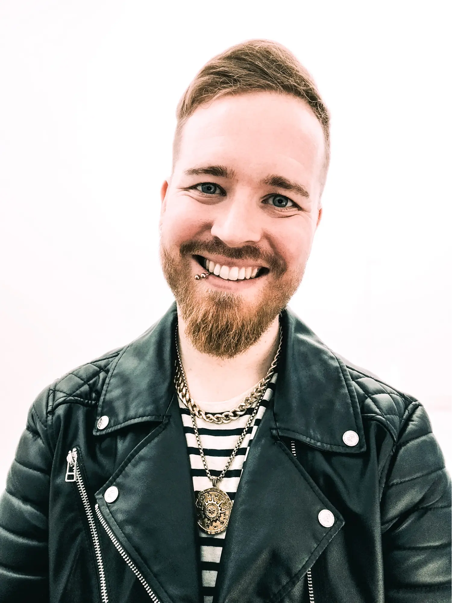 Porträt von Benjamin Chrubasik, Experte für Conversion Copywriting & Website-Strategie, lächelnd mit Bart und Piercing vor weißem Hintergrund. Das Foto zeigt ihn in einer schwarzen Lederjacke. Er ist Teil des Netzwerkteams der isi-Netzwerkagentur.