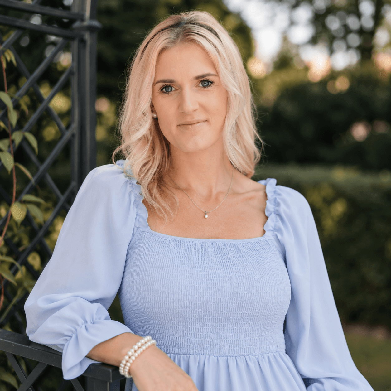 Porträt von Isabelle de Kort, Copywriterin bei der isi-Netzwerkagentur, mit blonden Haaren und einem hellblauen Kleid, fotografiert im weichen Sonnenlicht im Garten. Sie ist Teil des Netzwerkteams der isi-Netzwerkagentur.