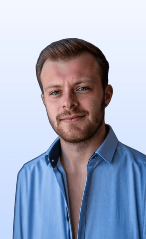 Porträt von Lukas Kraus, Ads Partner, lächelnd mit Bart und Kurzhaarschnitt vor neutralem blauem Hintergrund. Er ist Teil des Netzwerkteams der isi-Netzwerkagentur.