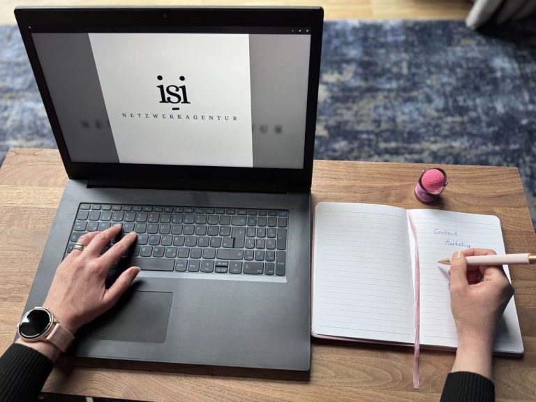 Ein Laptop mit einem Notizbuch und einer Hand, die gerade Notizen macht.